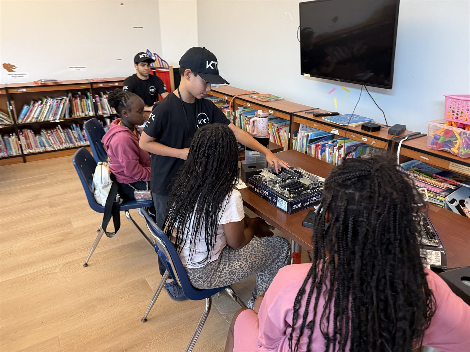 A teacher pointing at a motherboard for two campers at a library table