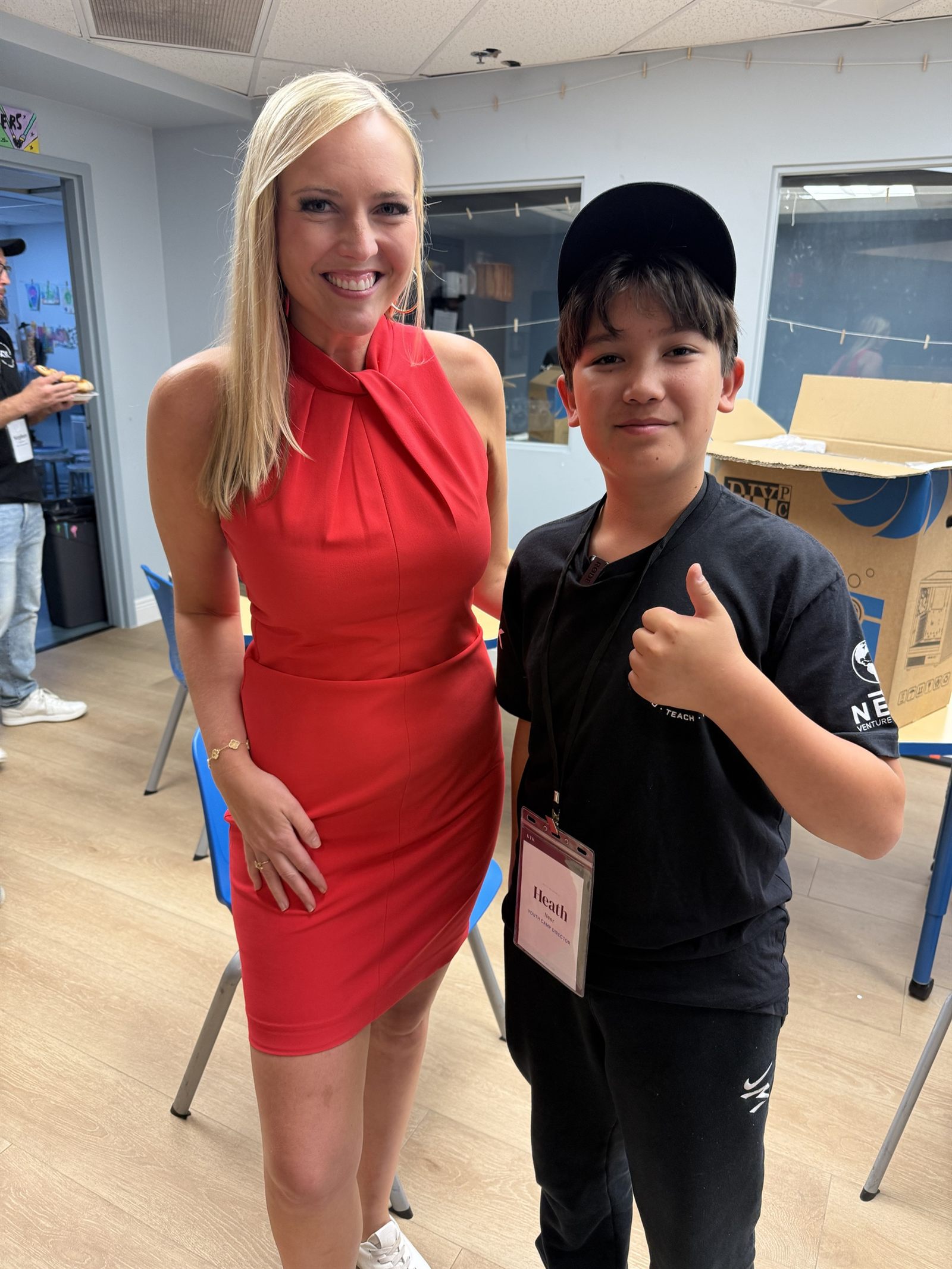 A TV reporter in a red dress with Heath, who is giving a thumbs up