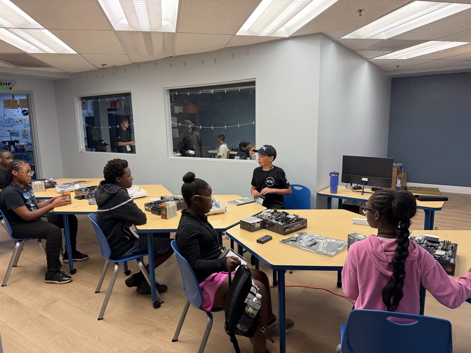 A teacher in a KTK cap talking with campers at a table of parts
