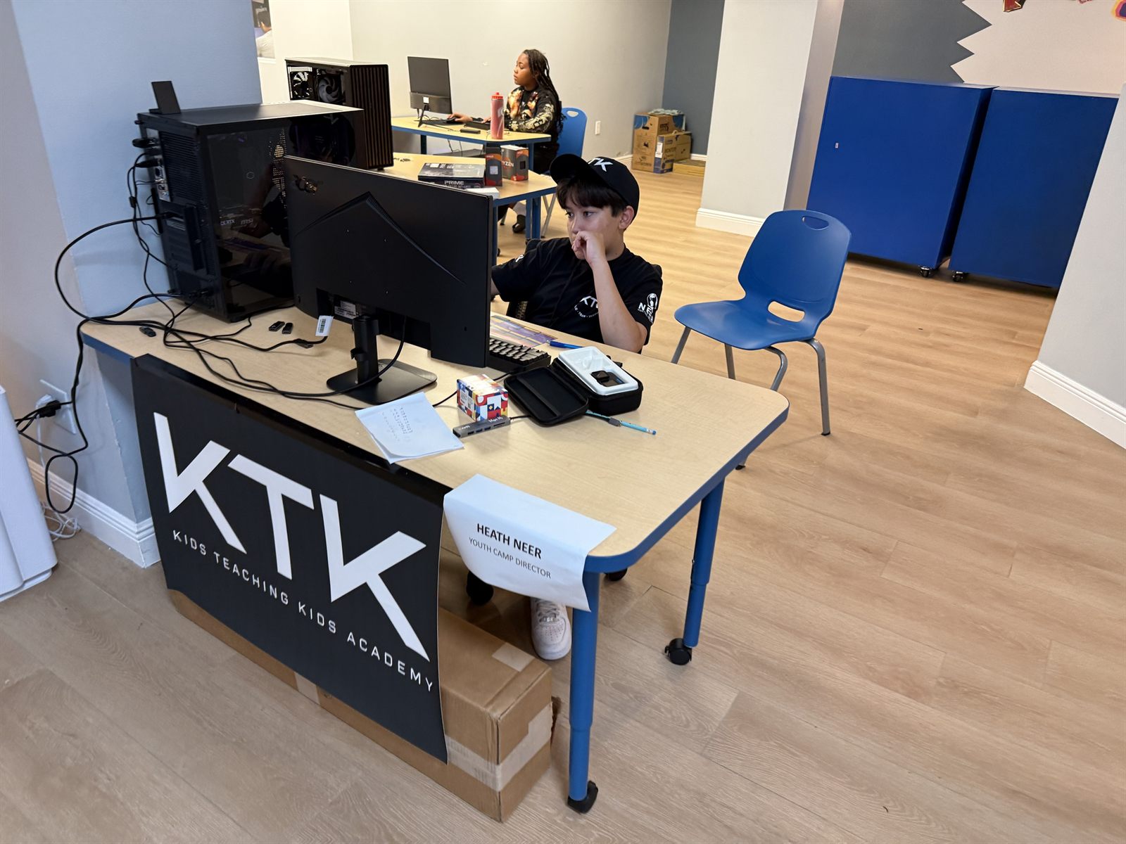 Heath at the camp director's desk with a KTK banner and a sign reading Youth Camp Director