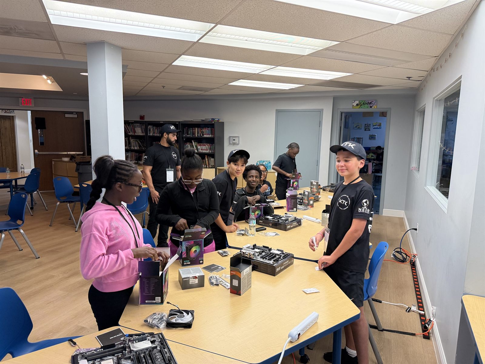 Campers and a teacher around a table opening cooler and motherboard boxes